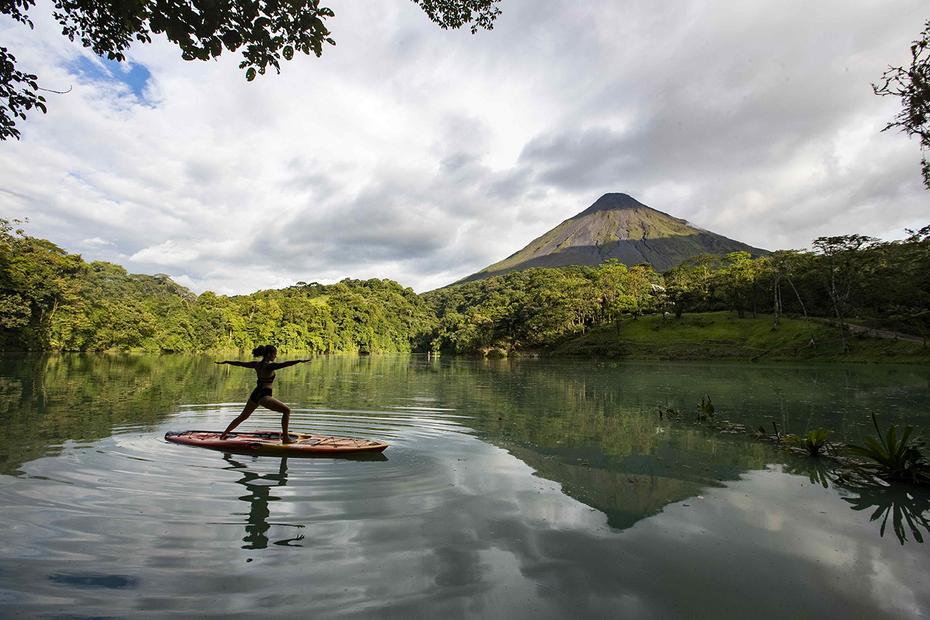 Una mujer practica yoga en una tabla en una laguna desde donde se aprecia el volcán Arenal, en la zona de la Fortuna de San Carlos, el 28 de agosto de 2020. EFE/Jeffrey Arguedas