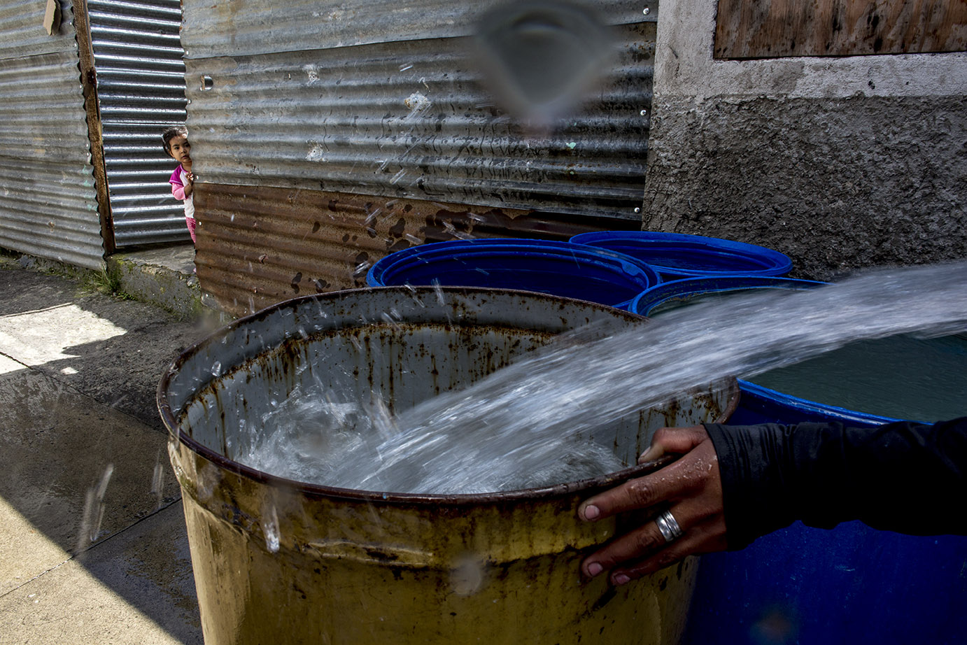 Una niña observa a un empleado de Empagua llenar un tanque de agua, desde la puerta de su casa, en la colonia Holanda, El Limón, zona 18, en noviembre 2019. Simone Dalmasso