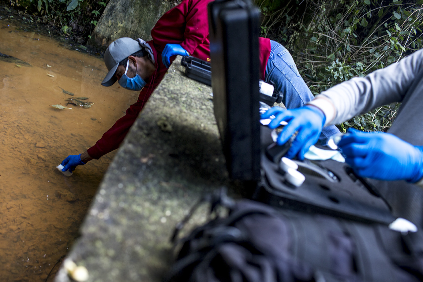 Fredy Joel García, 21, se dobla encima del muro de contención del tanque para agarrar una muestra de agua. Simone Dalmasso